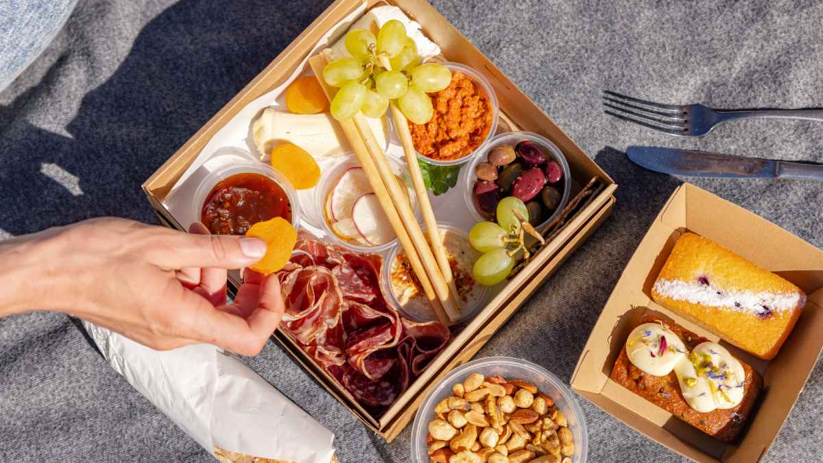 person picking up a dried apricot slice from a picnic box