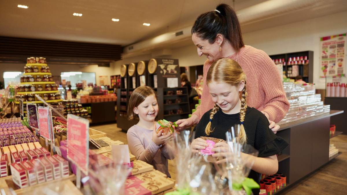 mother and two daughters smiling and looking at chocolate products in a store