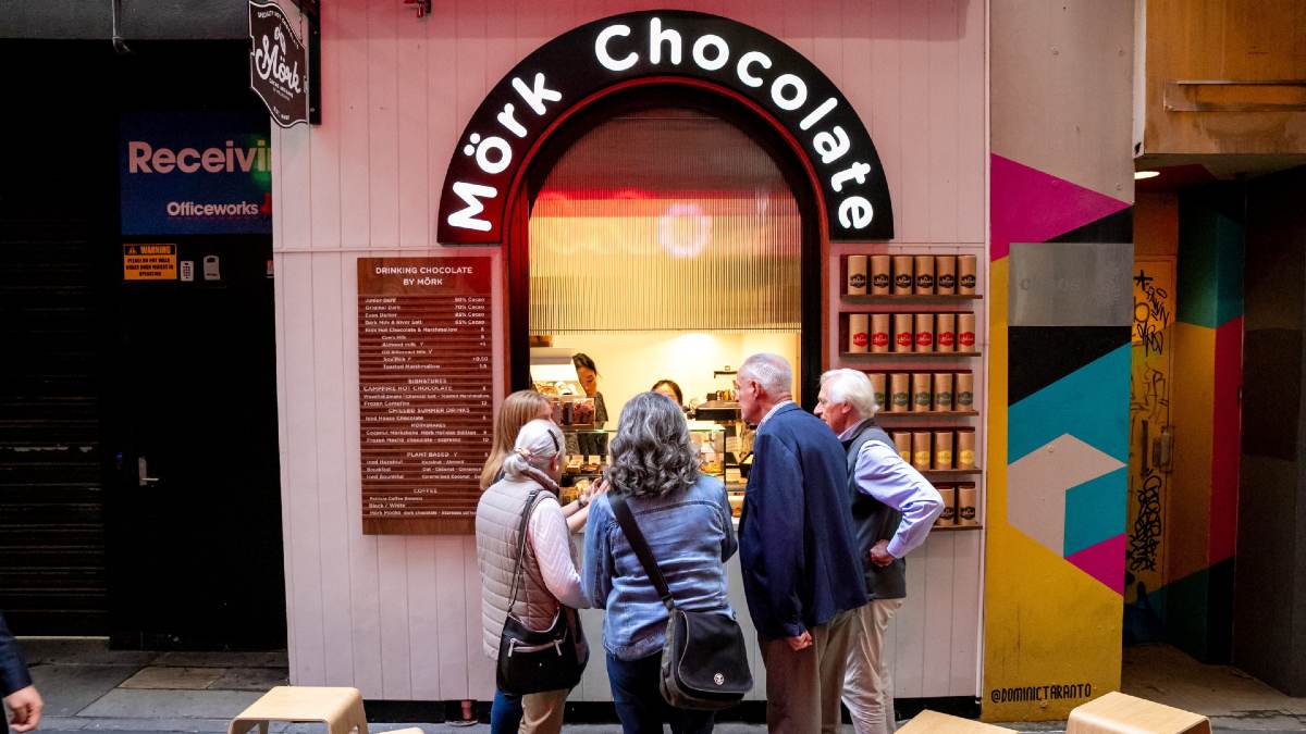 four people gathering around a chocolate shop window