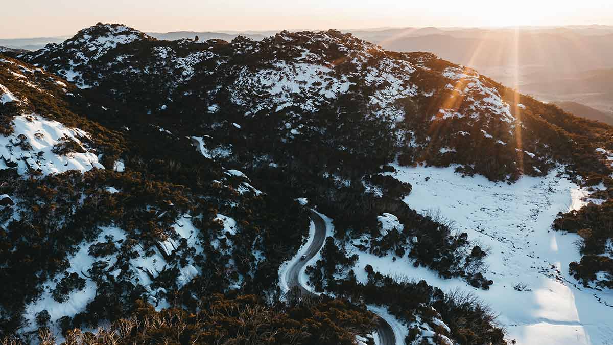 Aerial view of Mount Buffalo in winter at sunrise, with snow covered forest and winding road