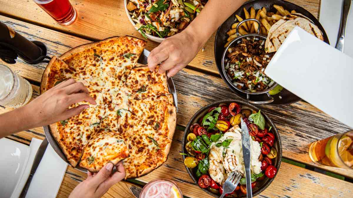 people reaching for a pizza on a table full of pub dishes