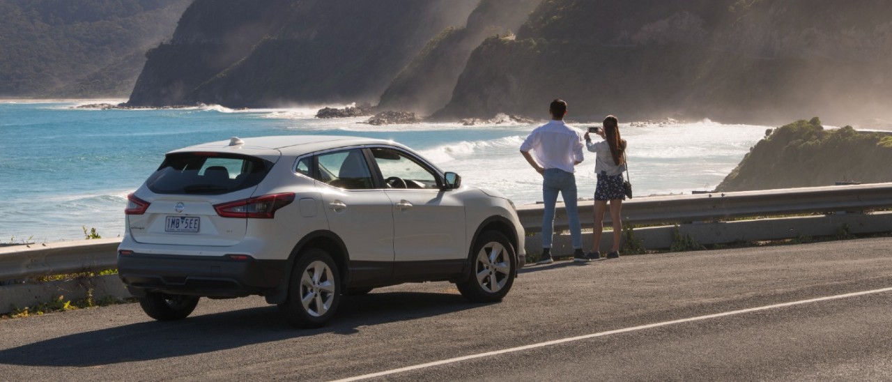 A couple admiring the ocean from the Great Ocean Road while their white SUV car is parked nearby