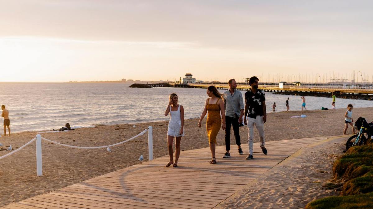 A group of young adults walking along the St Kilda foreshore (Bay Trail) at sunset on  warm day