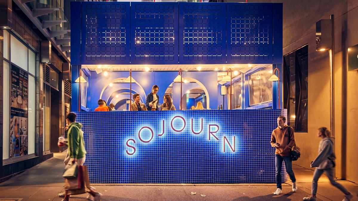 People walking past the bright blue laneway bar and restaurant, Sojourn, at dusk. 