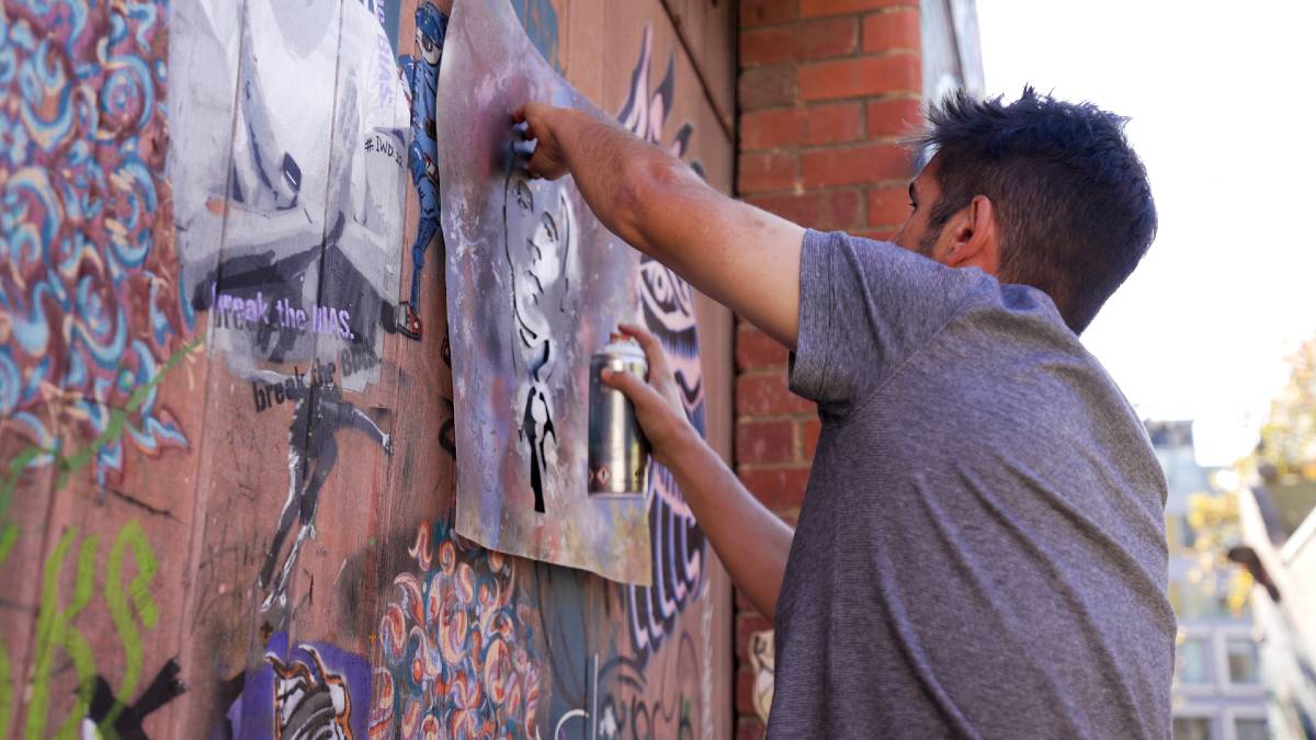 Street artist and director of Blender Studios, Doyle, using a stencil and spray paint to create a work on a brick wall in a laneway