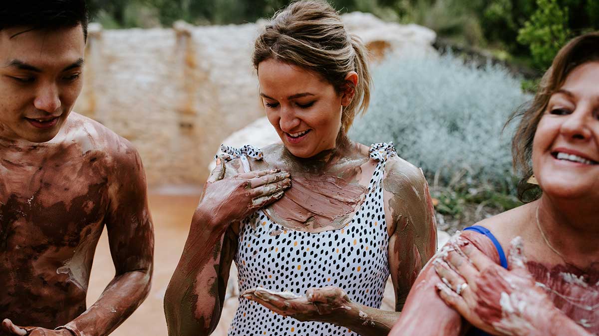 Three people put mud on their bodies as part of their hot springs experience on the Mornington Peninsula.