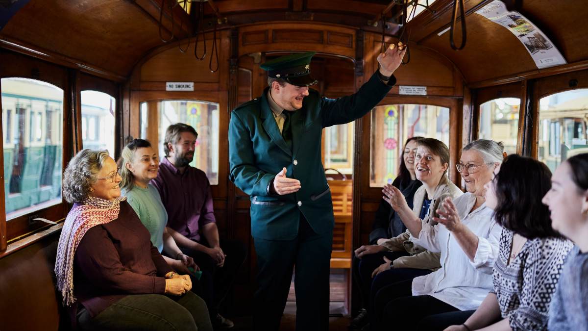 group of tourists sitting aboard an old tram listening to a uniformed conductor