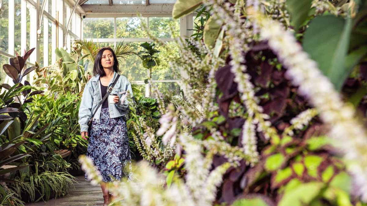woman holding a coffee and walking through a conservatory