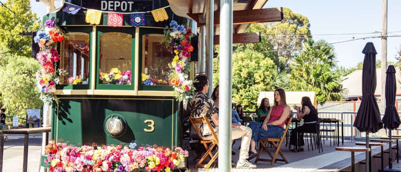 people sitting on a deck by a tram covered in flowers