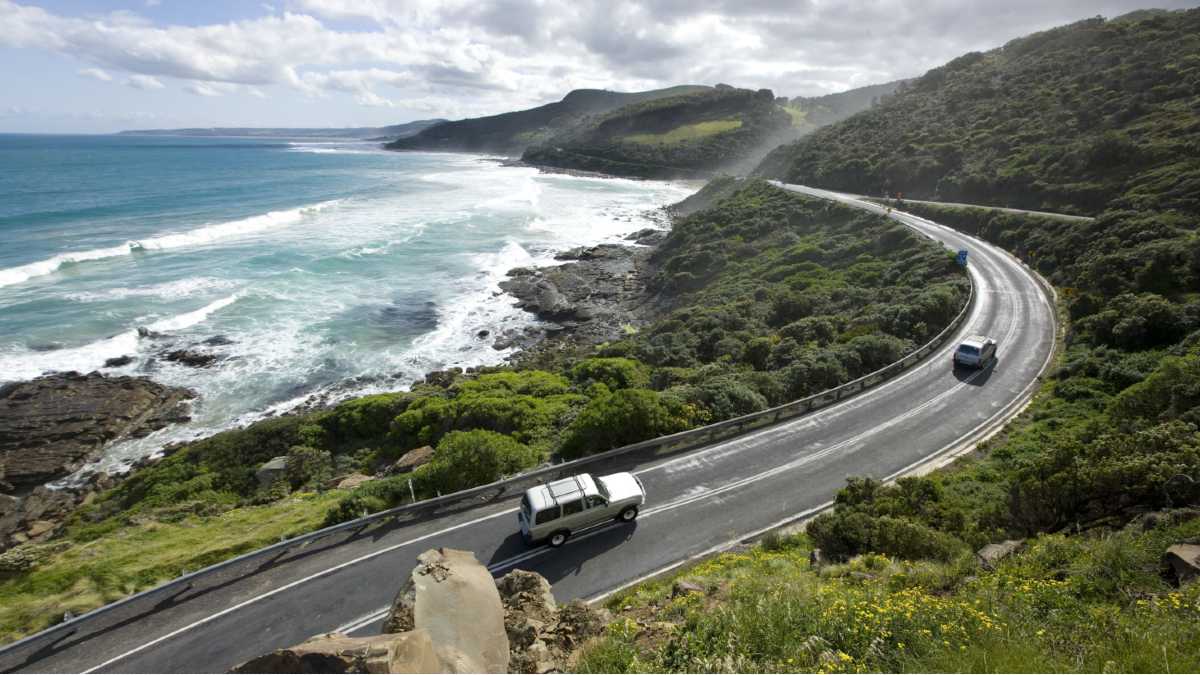 cars driving on road with ocean on left and rainforest on right