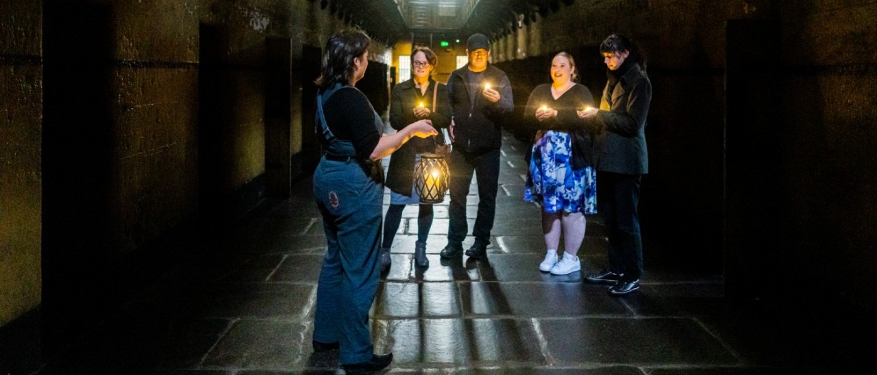tour guide leading candlelit ghost tour in an old gaol with four guests