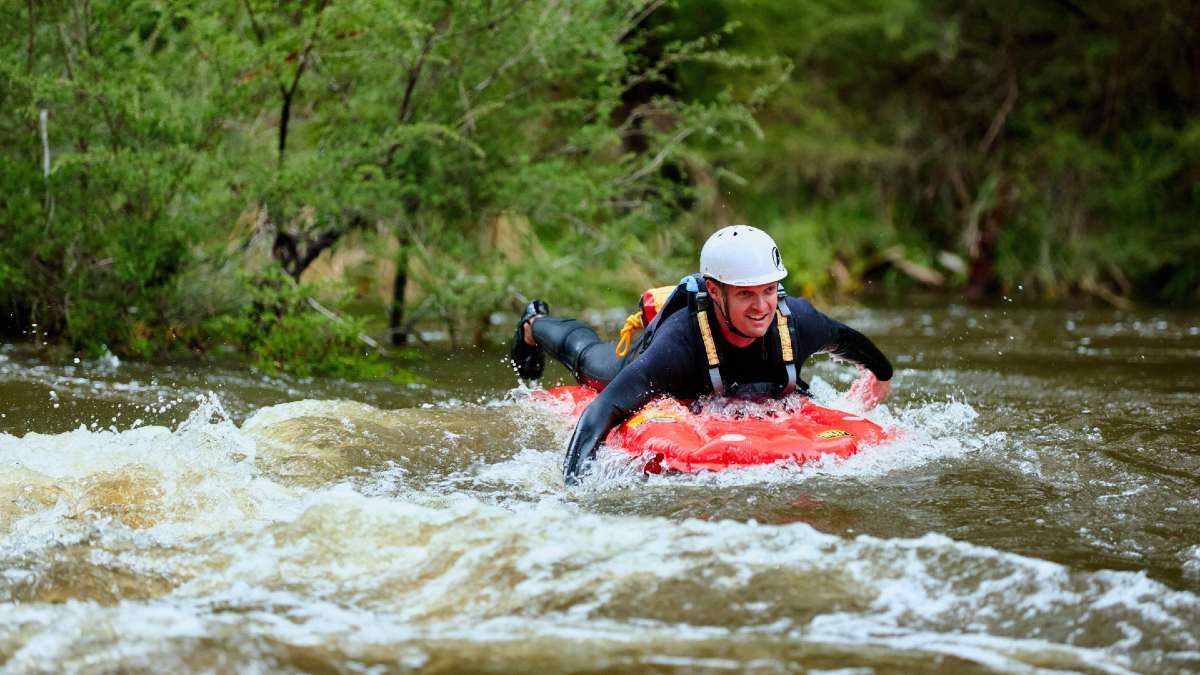 man paddling on inflatable raft in river wearing a wetsuit and helmet