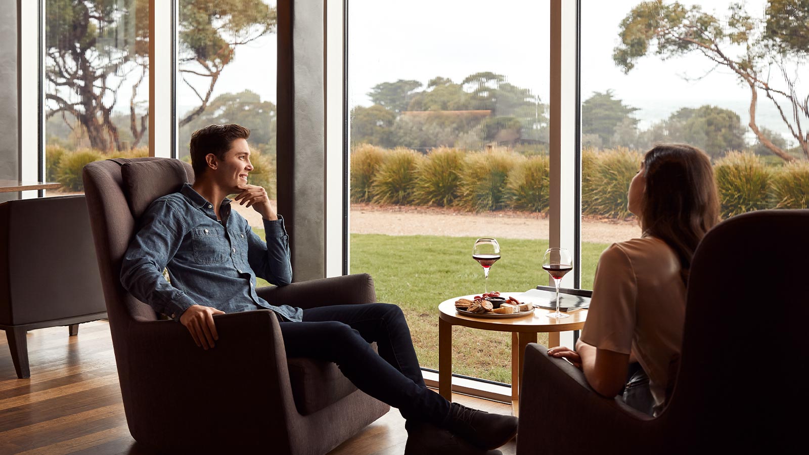 Couple seated with wine and snacks by a window at RACV Inverloch Resort.